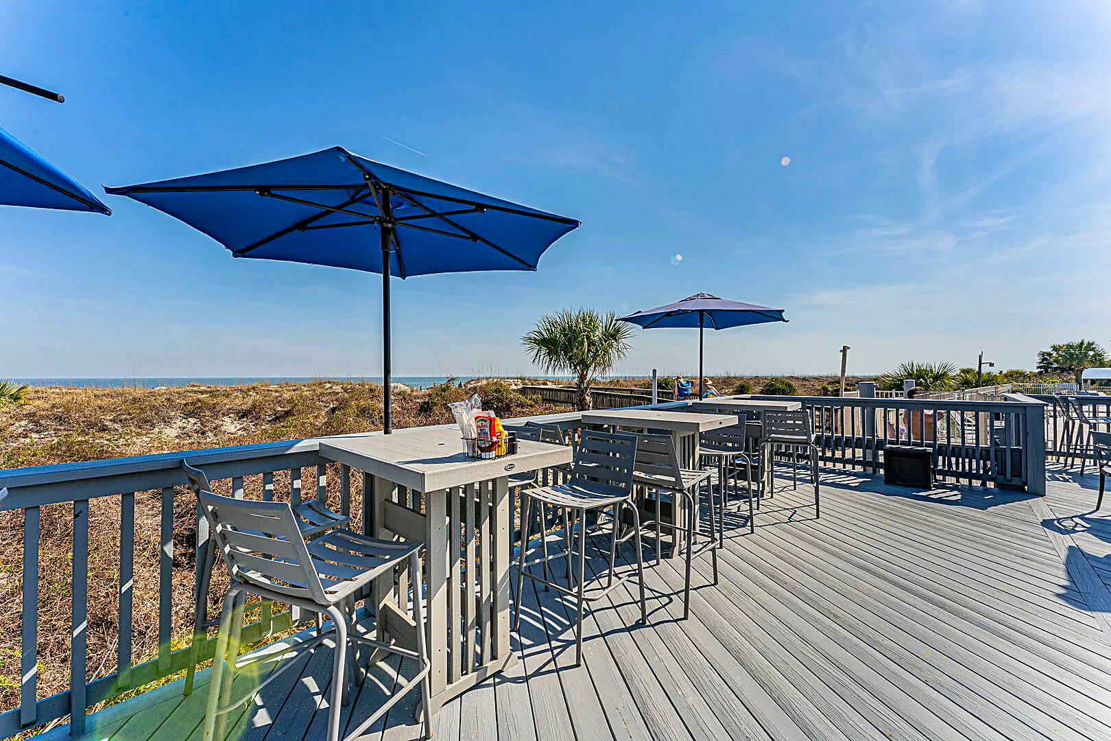 Oceanfront deck with blue umbrellas and high tables looking over the dunes to the Atlantic at 40 Folly Field Road, Hilton Head Island